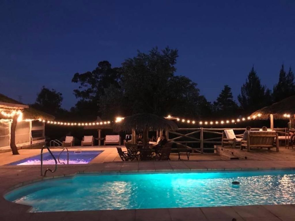 Piscinas iluminadas de noche con luces decorativas colgando sobre ellas en Rafaella ChacraEventos