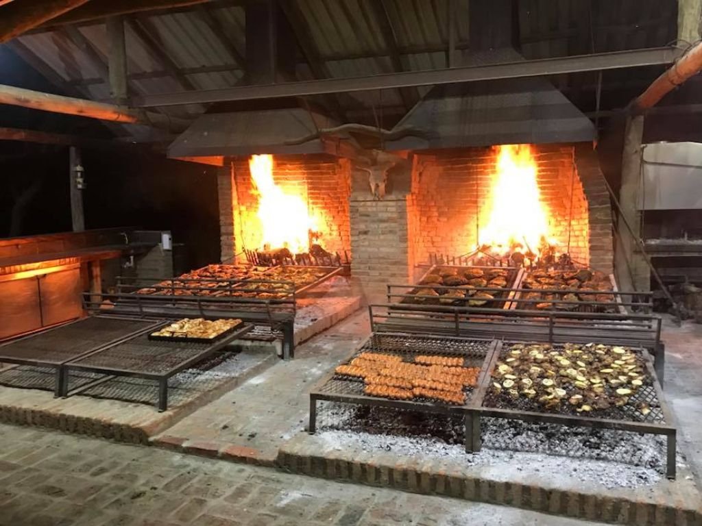Parrilla llena de carne y chorizos asándose en Rafaella ChacraEventos, lista para un deliciosa cena