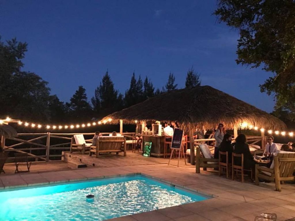 Piscina con quincho iluminado de fondo en Rafaella ChacraEventos, creando un ambiente acogedor y elegante
